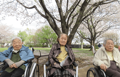 遅咲きの桜を背景に並ぶご利用者さま